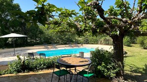 A pool area with a round table and chairs, surrounded by greenery and a tree. - Holiday Home in Villecroze with Pool & Garden (Villecroze)