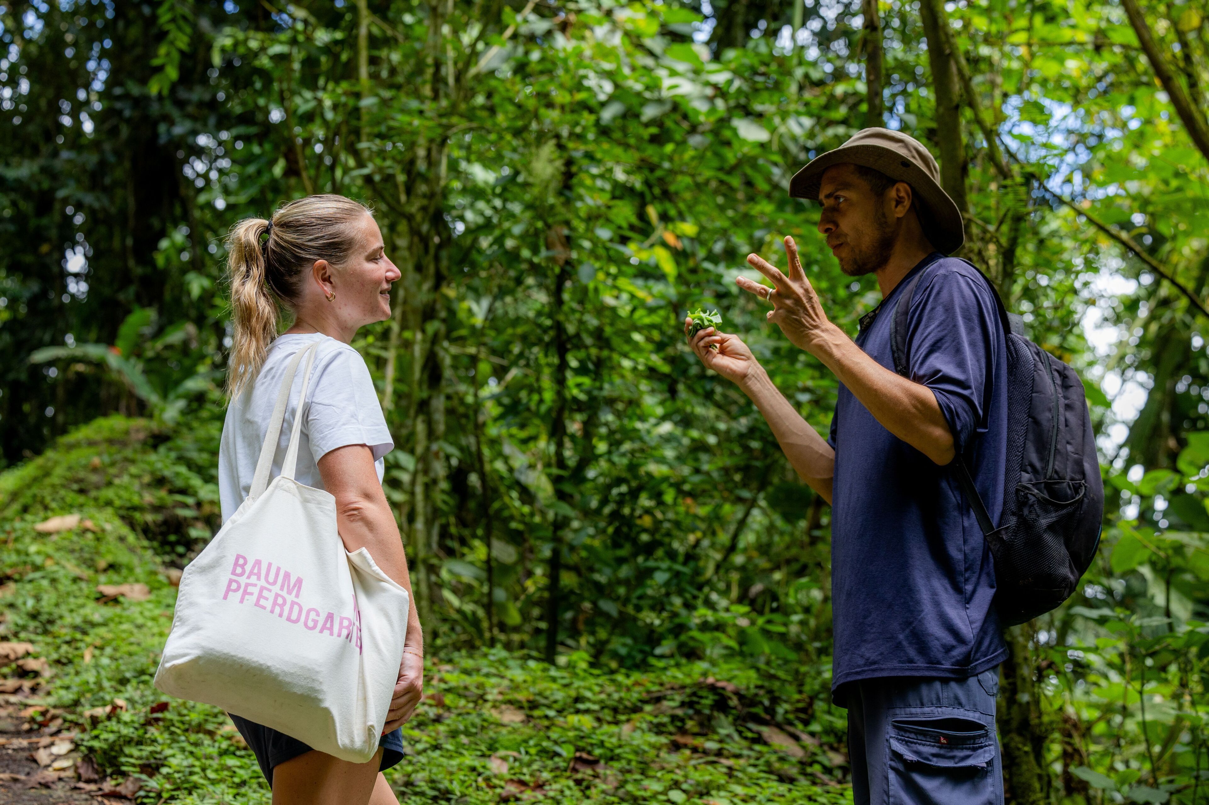 Dos personas en un área boscosa, una sosteniendo una planta.