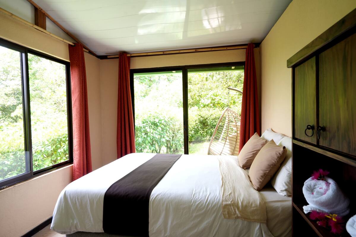 A bedroom with a bed, a wardrobe, and large windows with curtains.