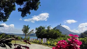 A paved pathway, lush greenery, a mountain, and a body of water.