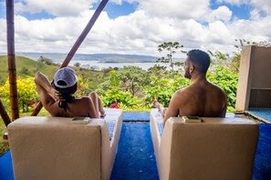 Two lounge chairs facing a pool with a view of a lake and hills. - Essence Arenal Spa & Yoga (Peñas Blancas)