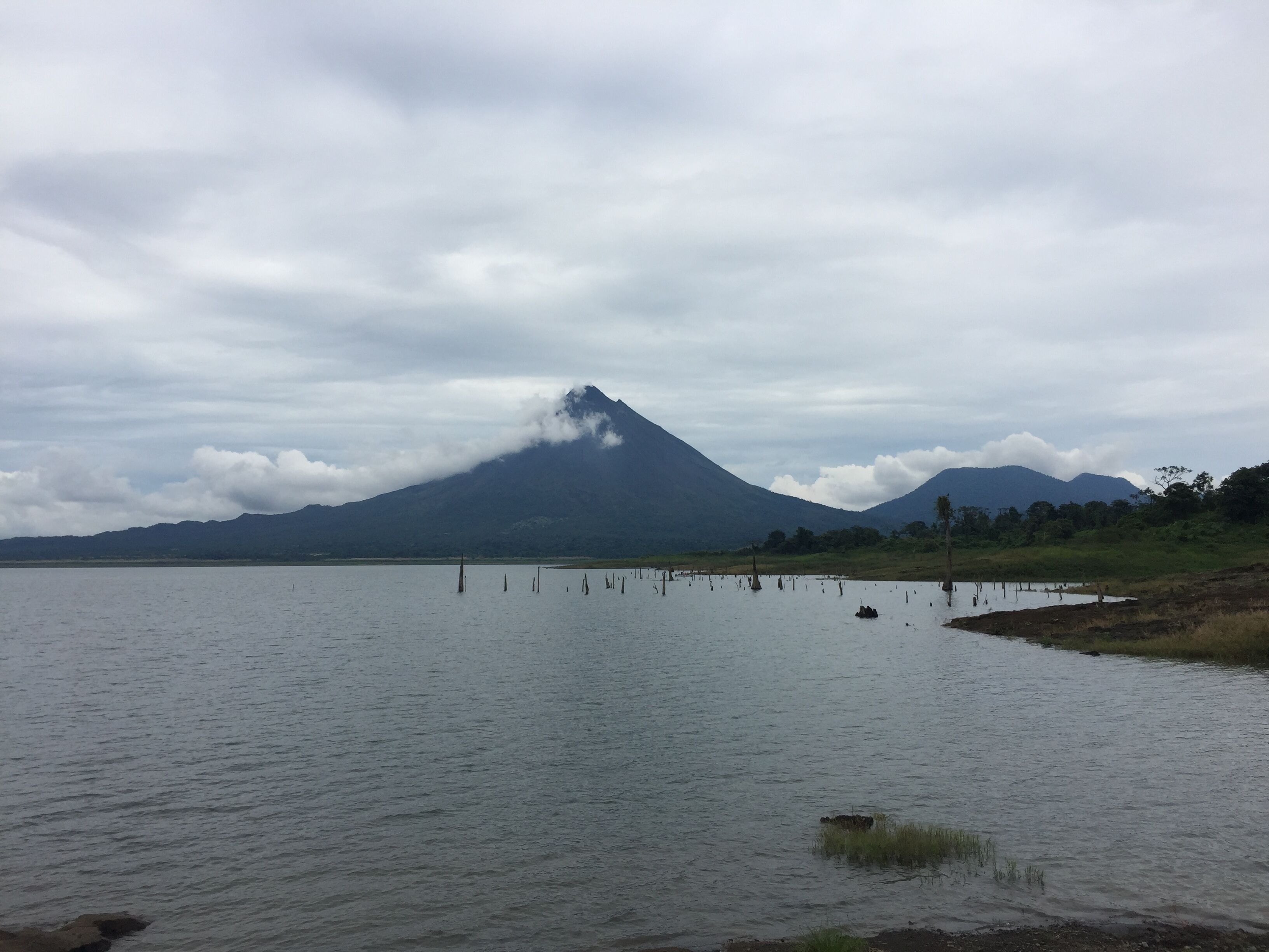 Ein See mit einem Berg im Hintergrund und bewölktem Himmel.