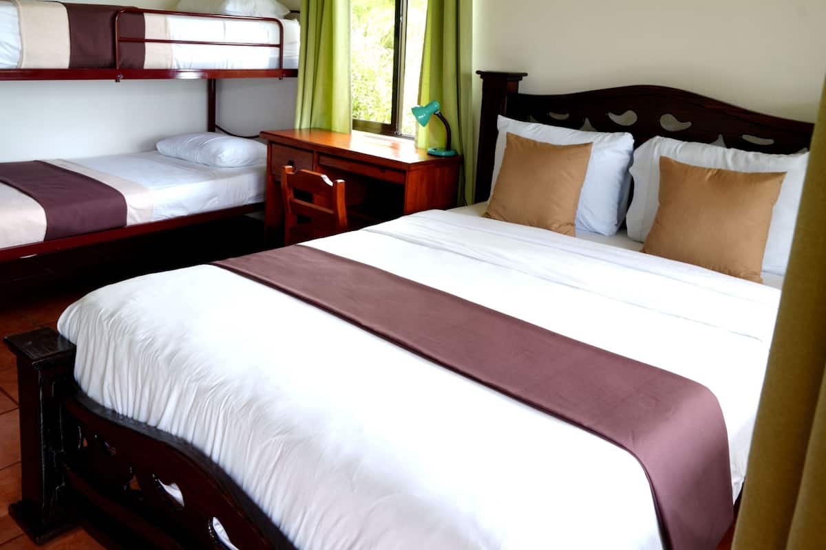 A hotel room with two single beds, a double bed, a desk, and a window with curtains.