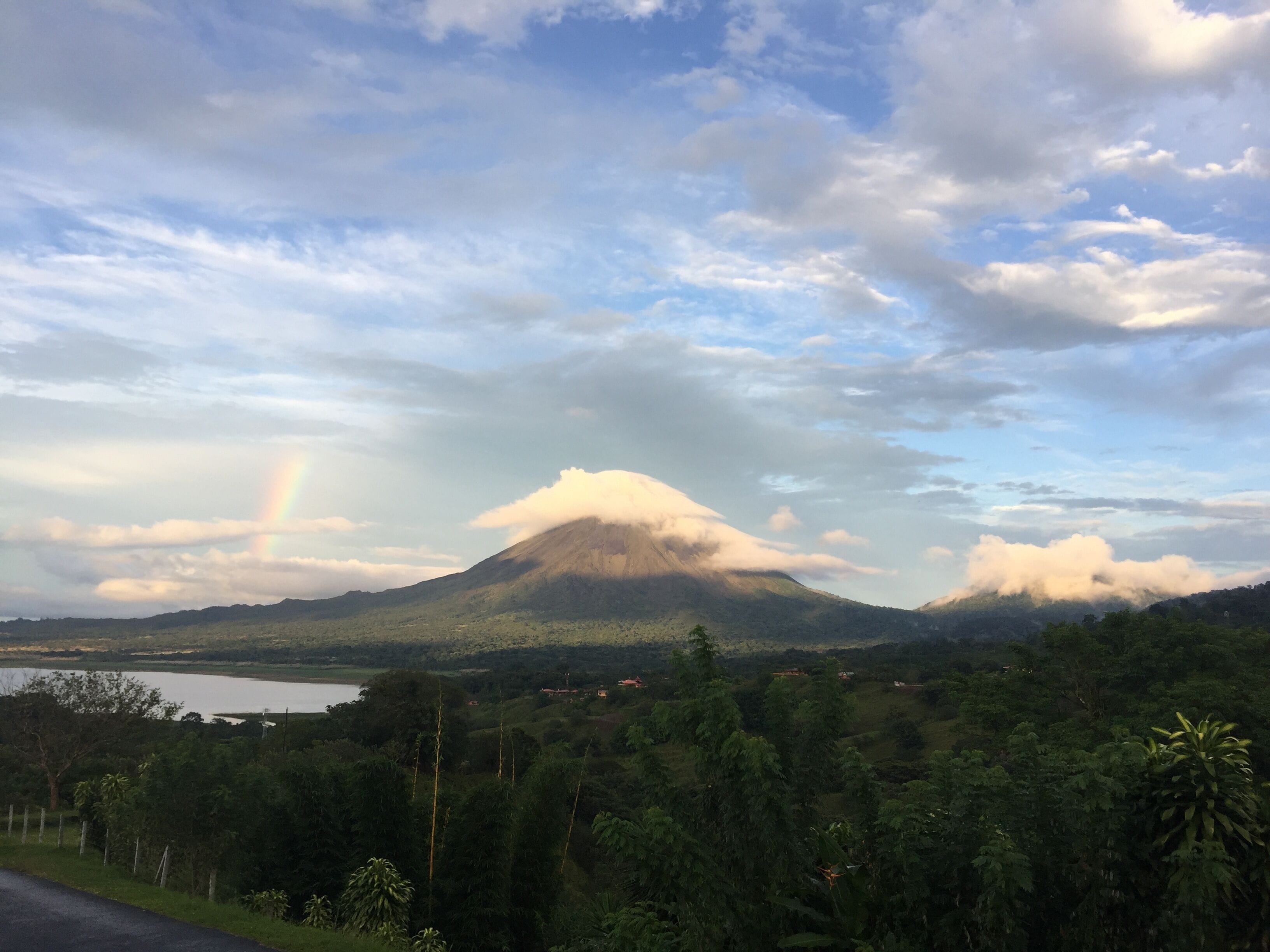 Ein Berg, darunter eine Wolkenbasis, ein Regenbogen und ein See im Vordergrund.