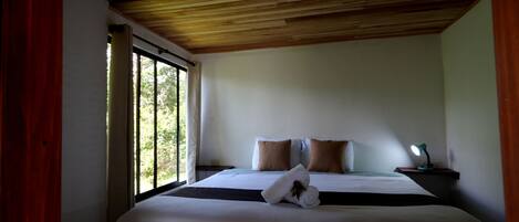 Um quarto com uma cama grande, uma mesa de cabeceira com abajur e uma janela com cortinas.