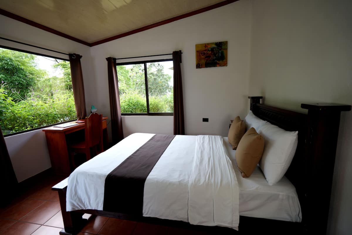 A bedroom with a bed, a desk, and a window with curtains.