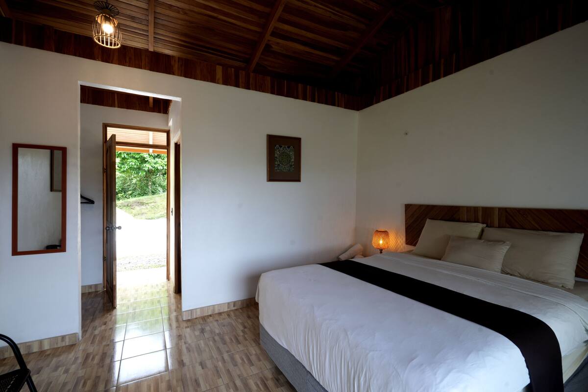 A bedroom with a bed, a bedside lamp, a framed picture, and a door leading to an outdoor area.