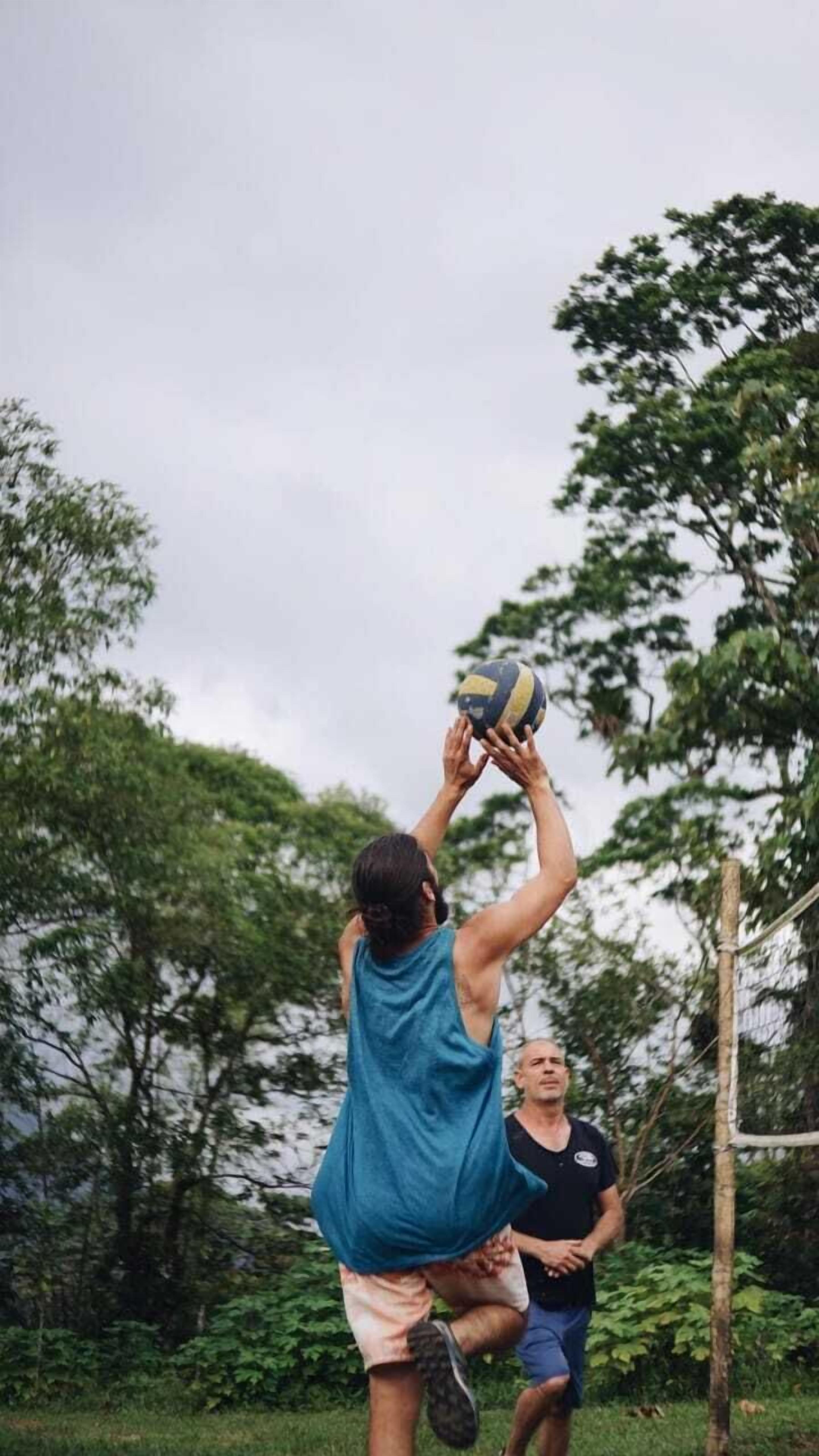 A person in a blue tank top jumping to hit a volleyball.