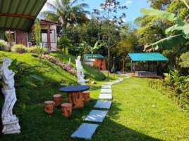 Um jardim com uma estátua, uma mesa com bancos, um caminho e um edifício com telhado verde.