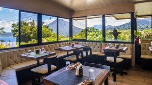A restaurant with multiple seating areas, large windows with a view of a mountain and a body of water.