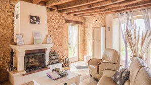 Une pièce rustique avec une cheminée, des murs en pierre, des poutres apparentes, un canapé blanc et une table à manger.