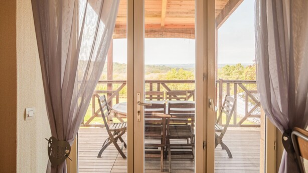 Une terrasse en bois avec une table et des chaises, une vue sur la verdure et un plafond en bois.