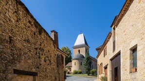 Une rue étroite bordée d’immeubles en pierre, une église dotée d’un clocher et un ciel d’un bleu limpide.