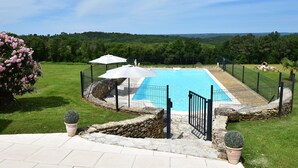 Une piscine bordée de pierres, entourée d’une clôture et agrémentée de plantes en pot.