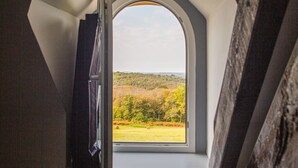 Une vue à travers une fenêtre à cadre triangulaire, dévoilant un paysage avec des arbres et un ciel dégagé.