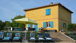 A yellow building with blue shutters, a pool, and outdoor seating with umbrellas.