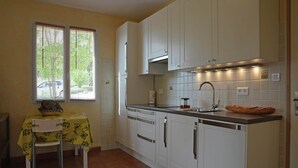 A compact kitchen with white cabinets, a tiled backsplash, and a window with blinds.