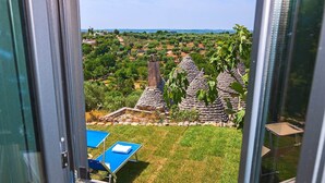 Blick aus einem Fenster auf eine ländliche Landschaft mit traditionellen Steingebäuden und einem Wiesenfeld.