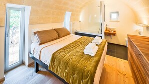 Ein Schlafzimmer mit einem Bett, einem Holzschrank, einem Fenster und einem Badezimmer mit Waschbecken und Spiegel.