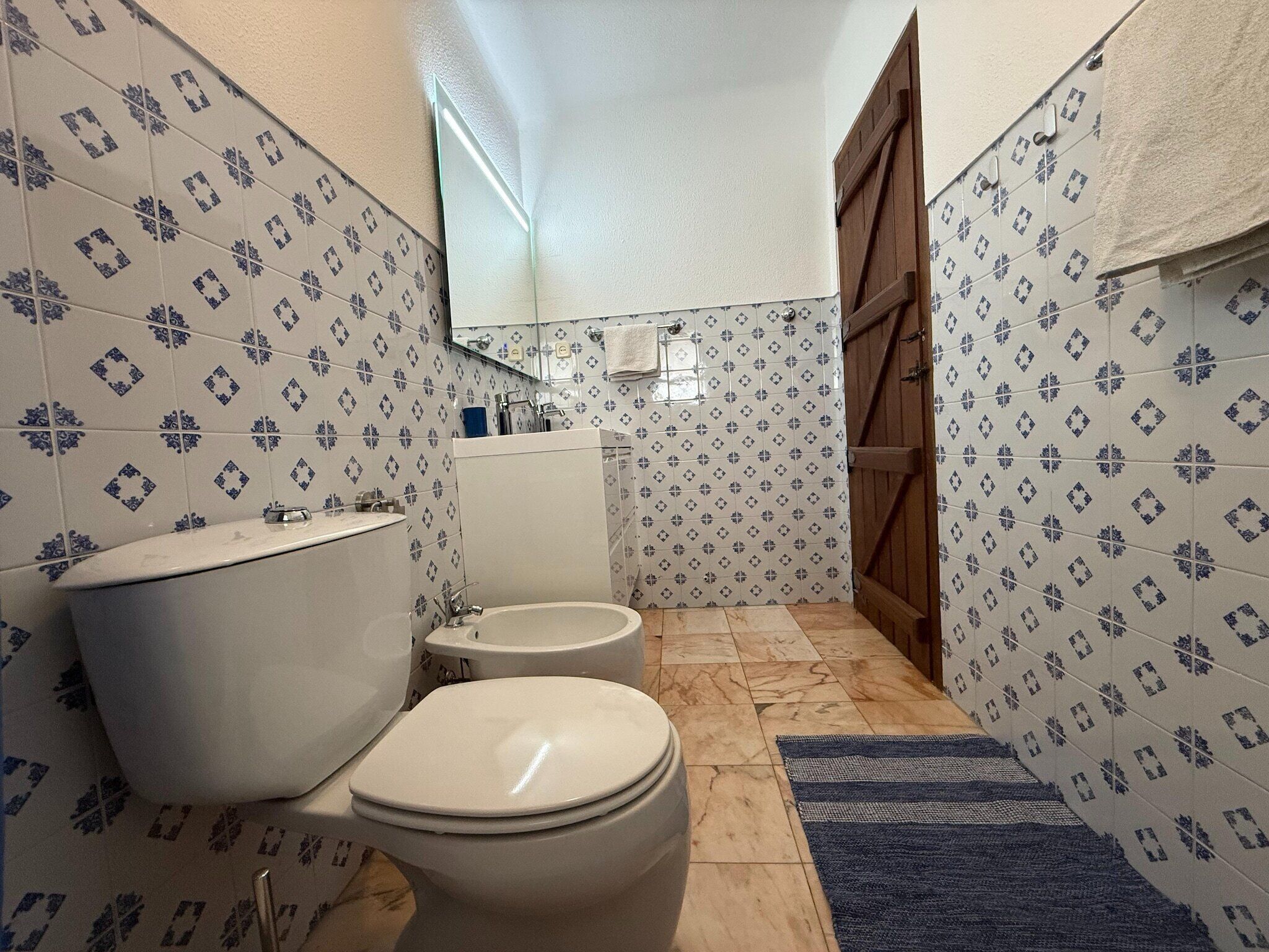 Un baño con inodoro, bidé y lavamanos, con paredes cubiertas de un diseño geométrico.