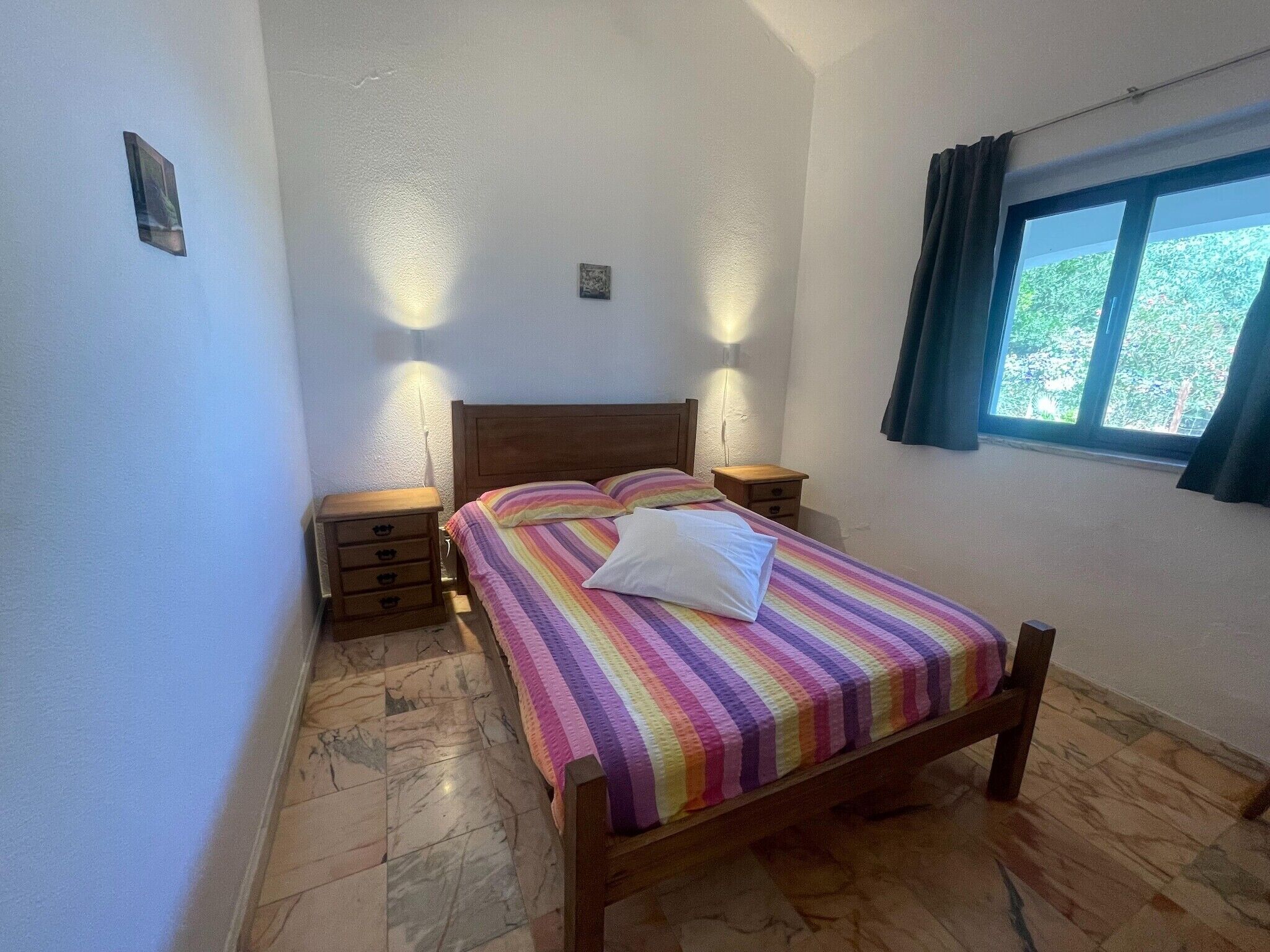 Een slaapkamer met een houten bed, een marmeren vloer en een raam met gordijnen.