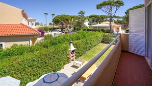 Un balcon donnant sur un jardin bien entretenu, un bâtiment blanc avec un toit recouvert de tuiles rouges et un ciel bleu dégagé.