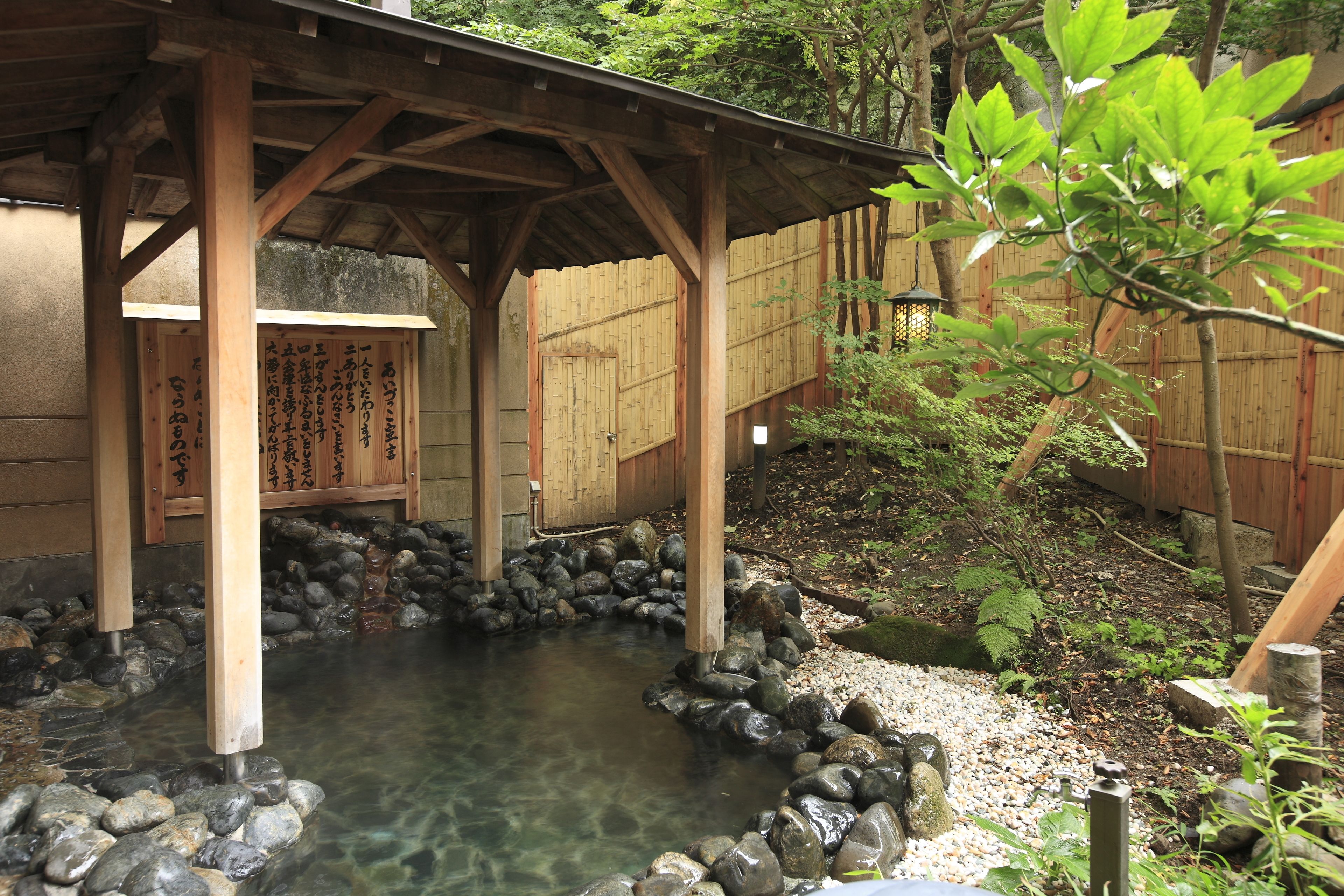 Un onsen japonés tradicional con estructuras de madera y una fuente termal cristalina.