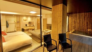 A modern hotel room with a large bed, a sitting area with a sofa and chairs, a small kitchen, and a wooden wall.