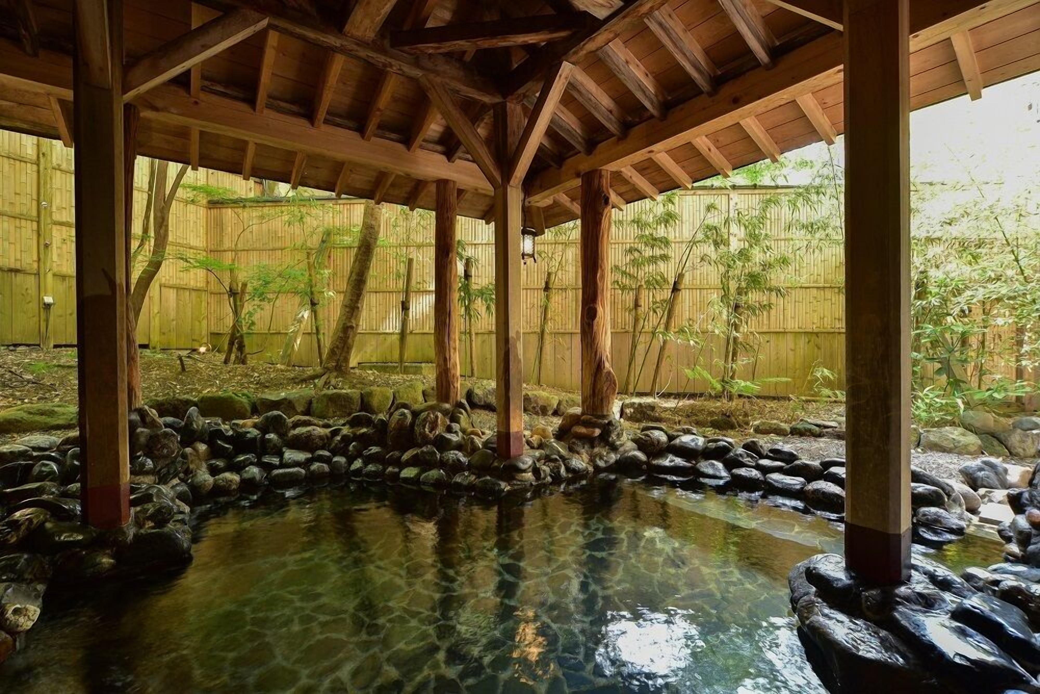 A traditional Japanese onsen with wooden beams and a bamboo fence in the background.