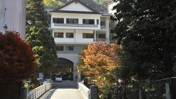 Un immeuble à plusieurs étages, doté d’une entrée centrale, entouré d’arbres et de voitures garées.