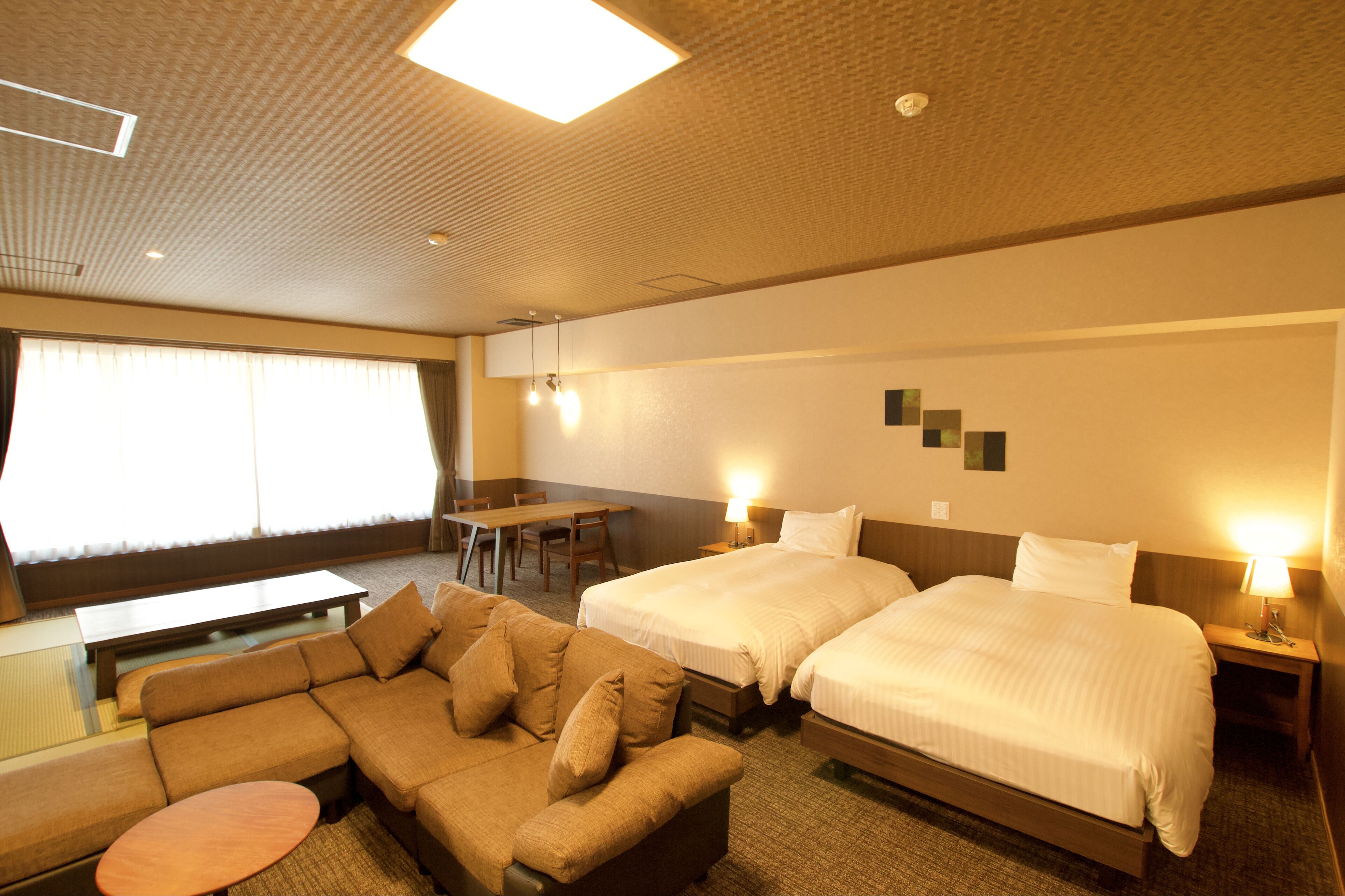 Een hotelkamer met twee bedden, een bank, een eettafeltje en een bureau.