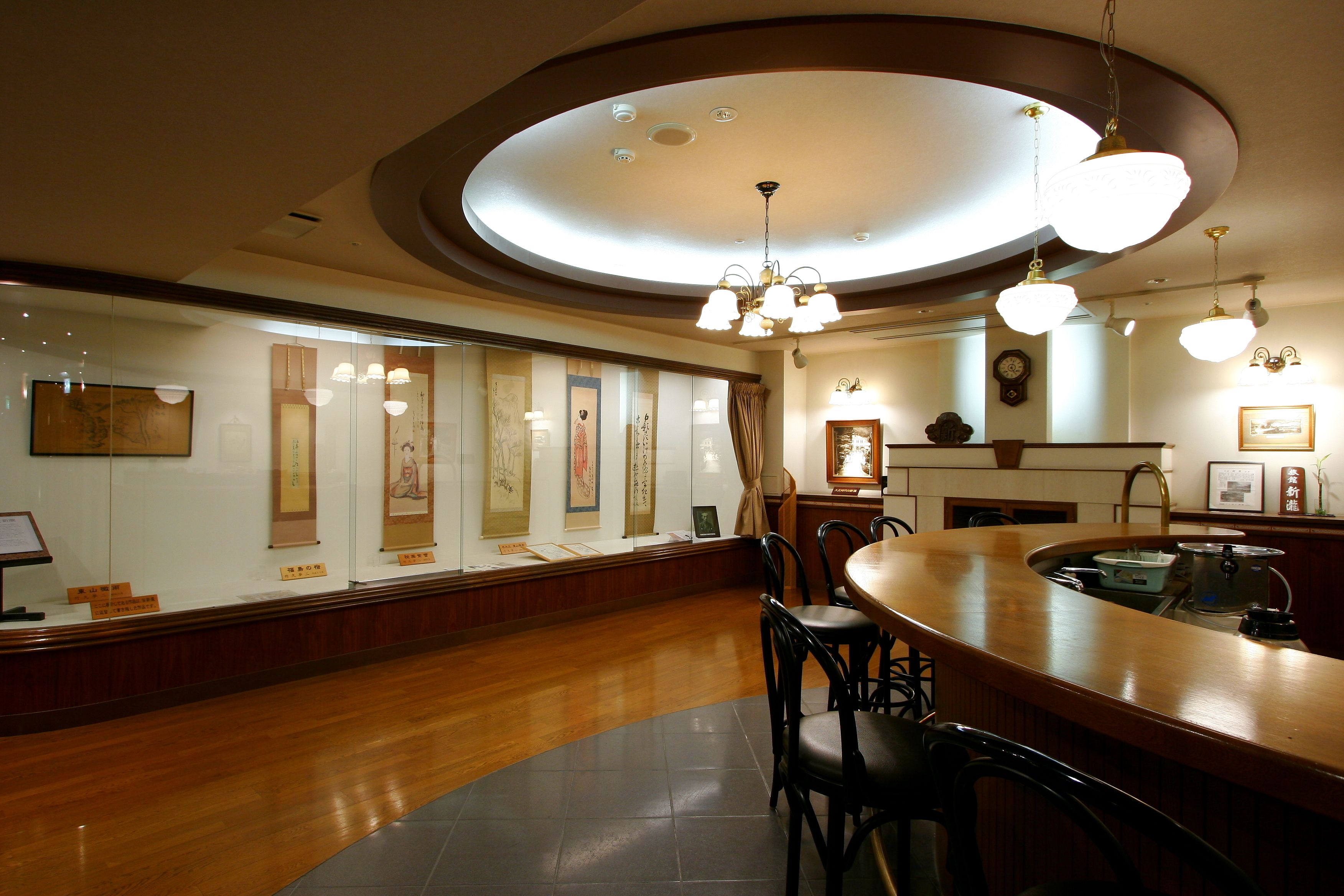 A restaurant with a wooden bar and chairs, a ceiling light fixture, and framed artwork on the walls.