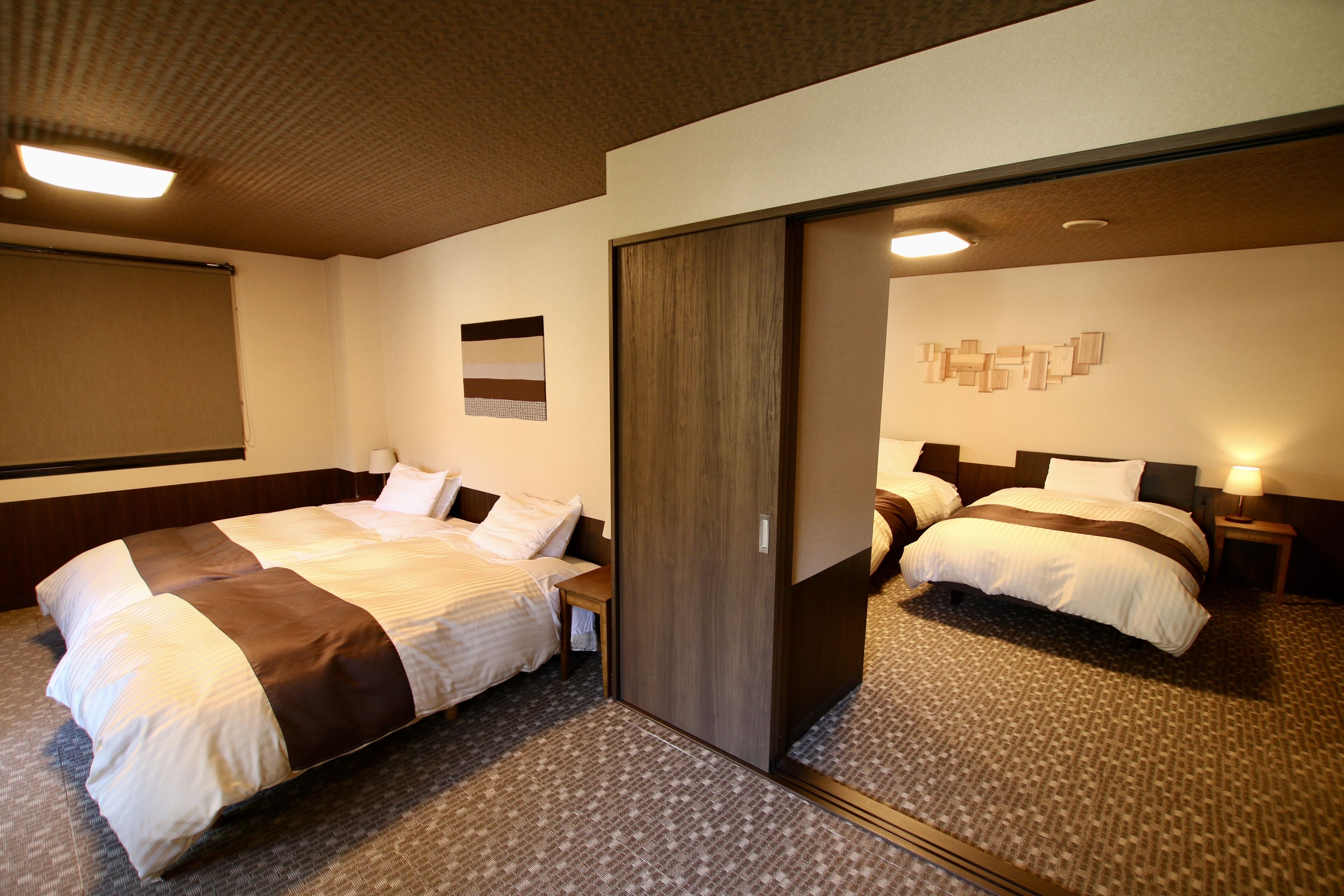 A hotel room with two beds, a wardrobe, a small table, and a wall-mounted artwork.