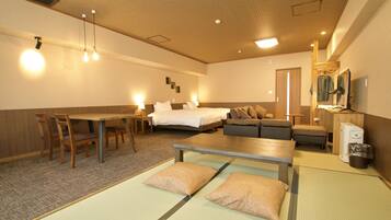 Habitación de hotel con cama, sofá, mesa de comedor, sillas y una pequeña kitchenette.