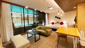 A modern hotel room with a bed, a sofa, a dining table, and a small table.