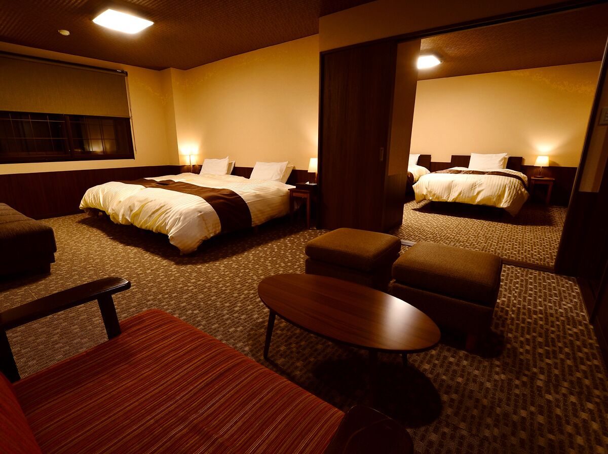 A hotel room with two beds, a sofa, a small table, and a carpeted floor.
