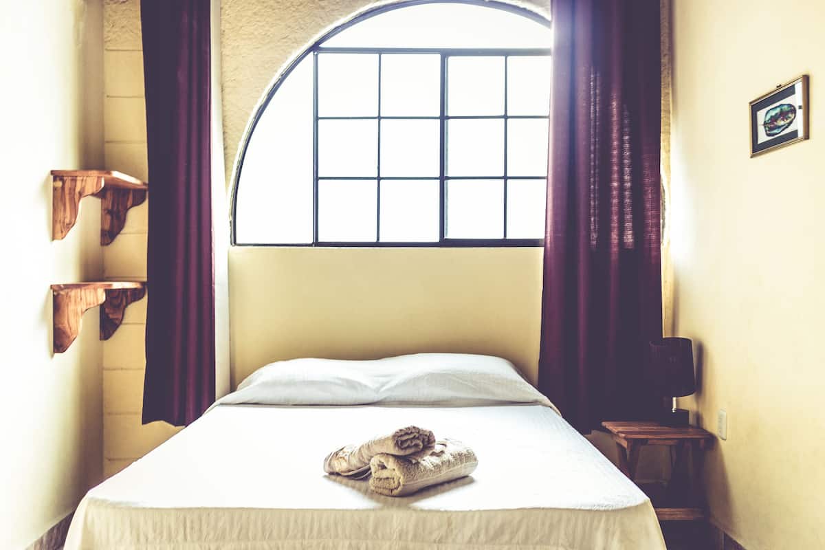 Un dormitorio con una cama, una ventana de diseño a cuadrícula, un estante de madera y una lámpara sobre una mesita de noche.
