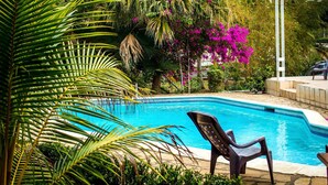 A swimming pool surrounded by lush greenery and a chair. - Casa Inti (Managua)
