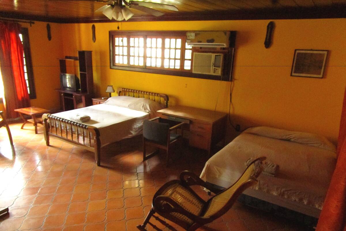 Una habitación con cama, escritorio, silla, televisor y aire acondicionado.