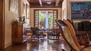 A room with a tiled floor, wooden furniture, a desk with bottles, and framed artwork on the walls. - Casa Inti (Managua)