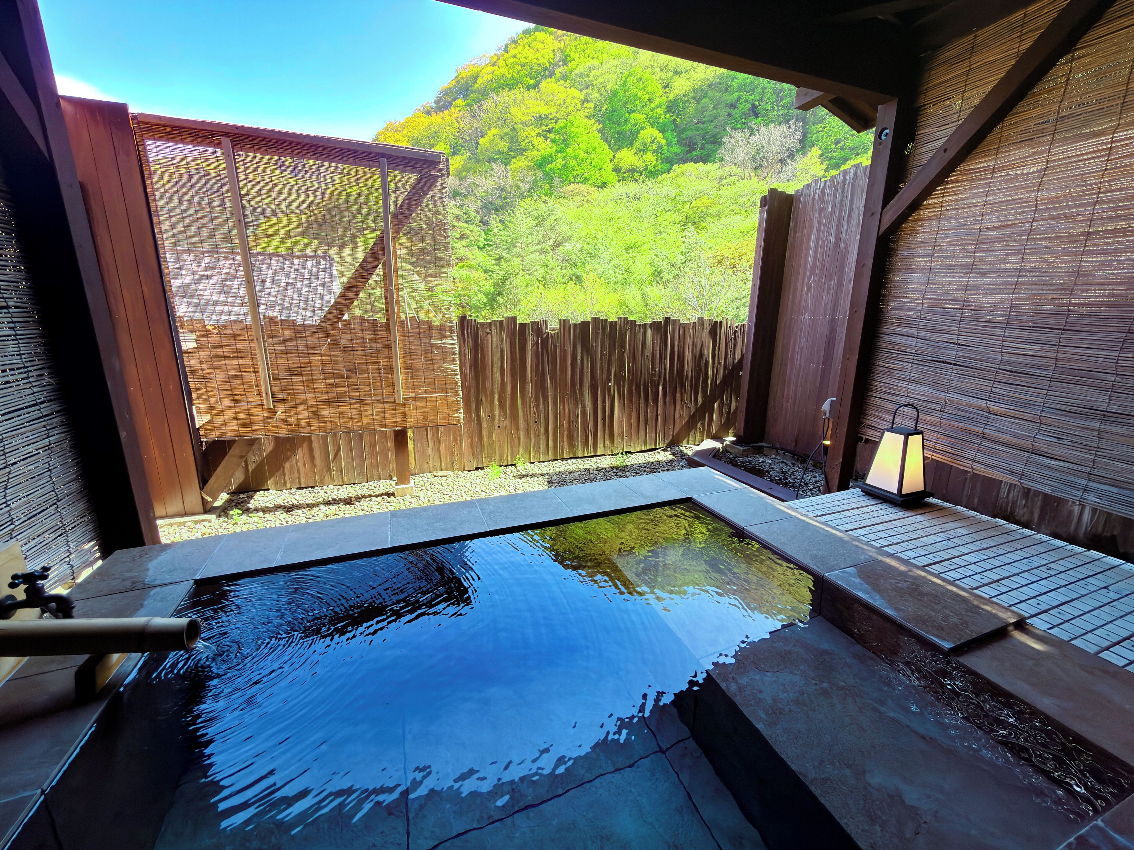 A hot tub with a wooden fence and a view of a green hillside.