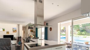 A modern kitchen with a central island, a dining area with a glass table, and a view of an outdoor swimming pool. - Villa in Vidauban near Sainte Maxime Beach (Vidauban)