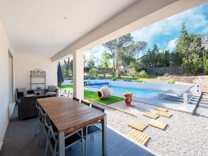 An outdoor patio with a wooden table and chairs, a small garden area, and a swimming pool. - Villa in Vidauban near Sainte Maxime Beach (Vidauban)
