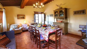 A dining area with a table set for four, surrounded by wooden chairs, a chandelier, and a cabinet with glass doors. - Escape to Vineyards, Elba (Radda in Chianti)