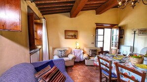 A cozy living room with a sofa, chairs, a dining table set for two, and a kitchen area with a radiator. - Escape to Vineyards, Elba (Radda in Chianti)