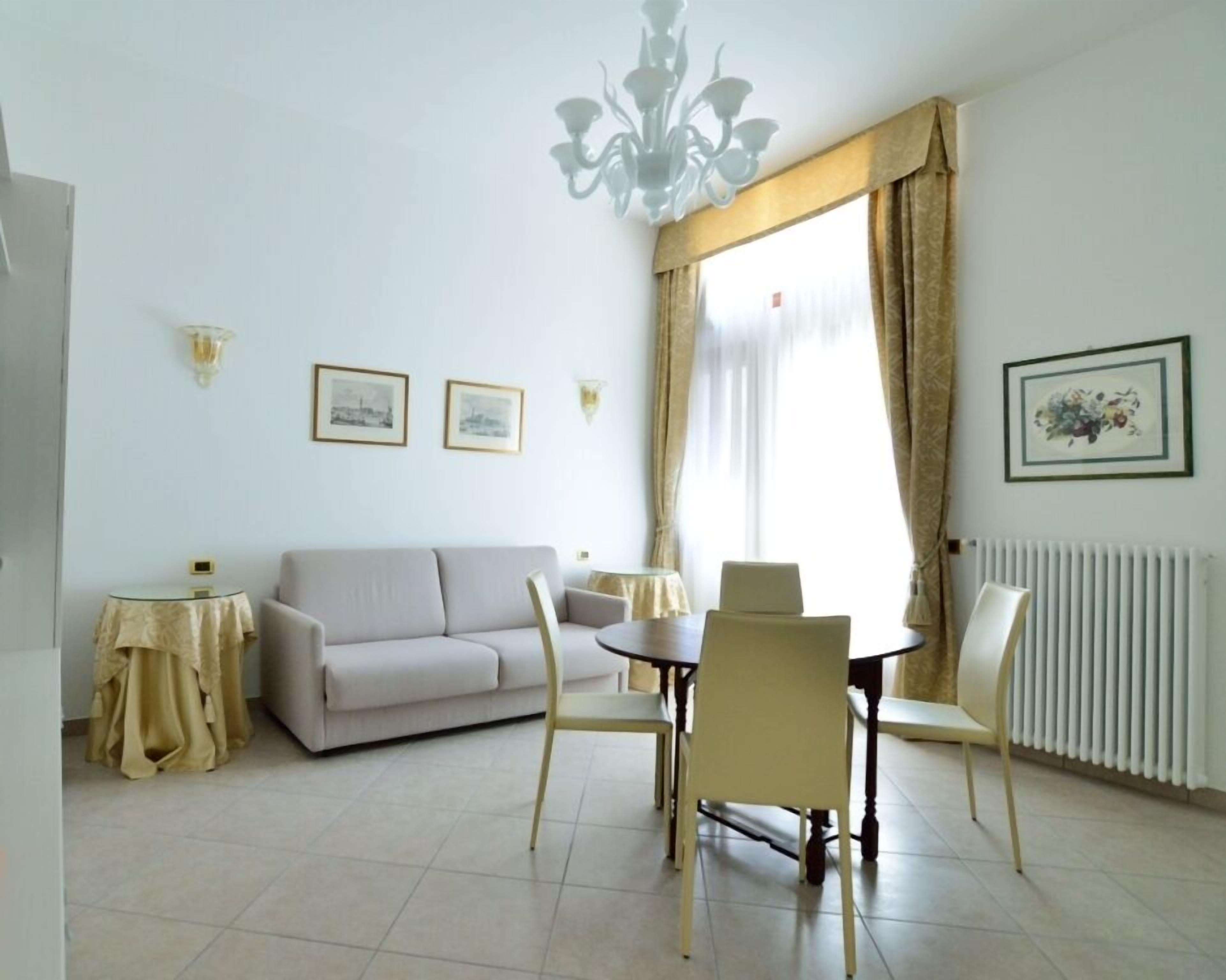 Een woonkamer met een bank, een eettafel, stoelen, een kroonluchter en ingelijste foto's aan de muur.