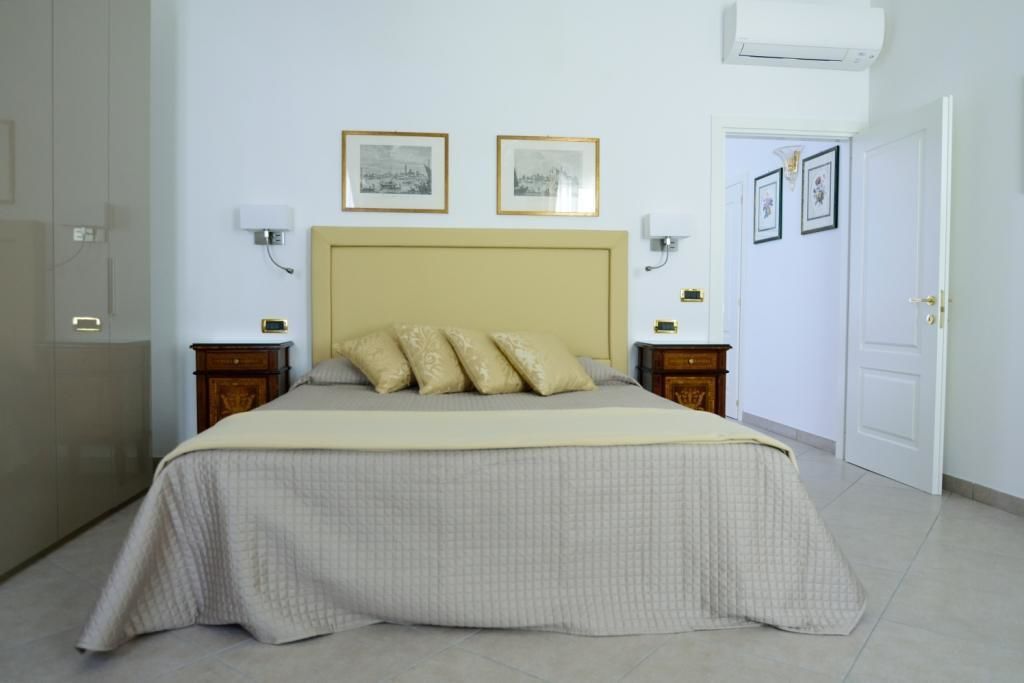 A bedroom with a bed, two bedside tables, a headboard, and two wall-mounted lamps.