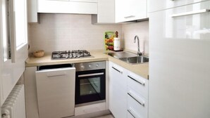 A compact kitchen with white cabinets, a gas stove, an oven, a sink, and a window. - Sissi Suite (Venice)