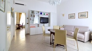 A modern living room with a sofa, dining table, chairs, a TV, and a bookshelf. - Sissi Suite (Venice)