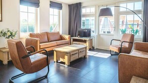 Una sala de estar moderna con un sofá, sillones, una mesa de centro, un televisor y ventanas grandes con cortinas.